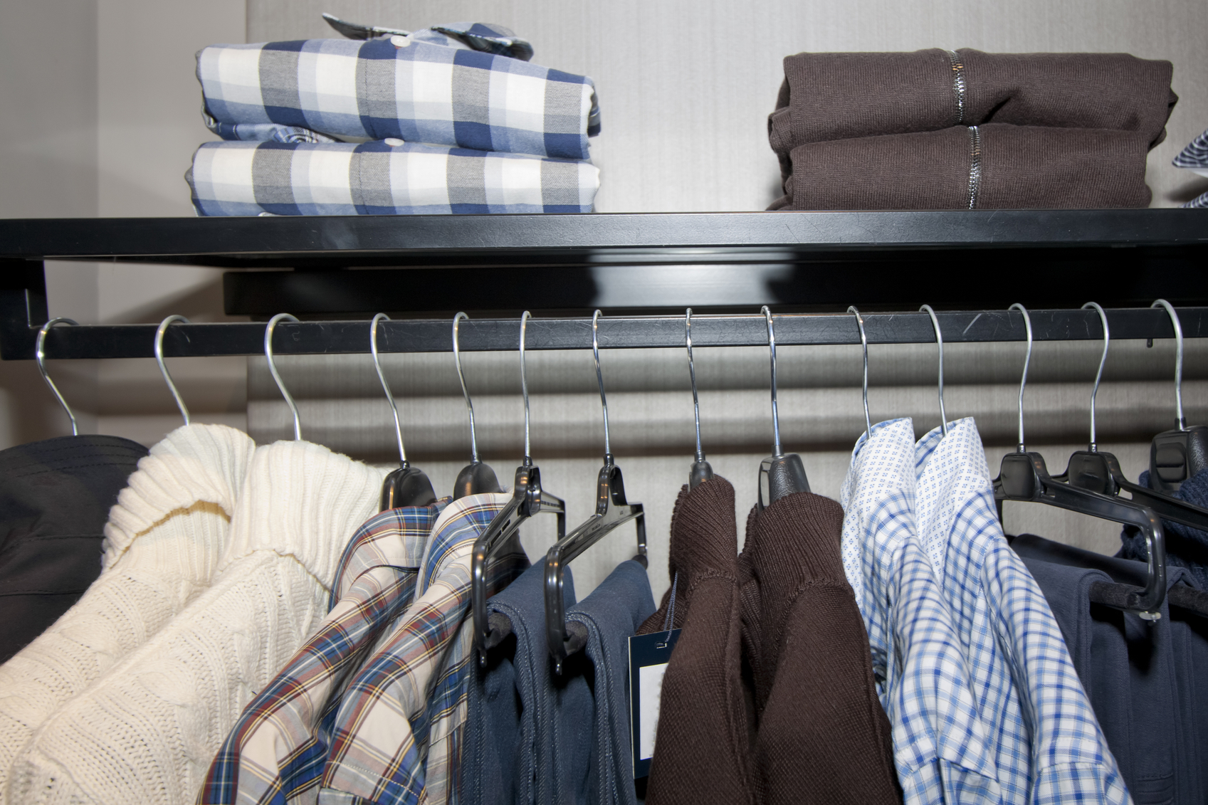 Close up of row of male clothes on hangers and folded on rack. Shirts, jeans,trousers,pullovers.