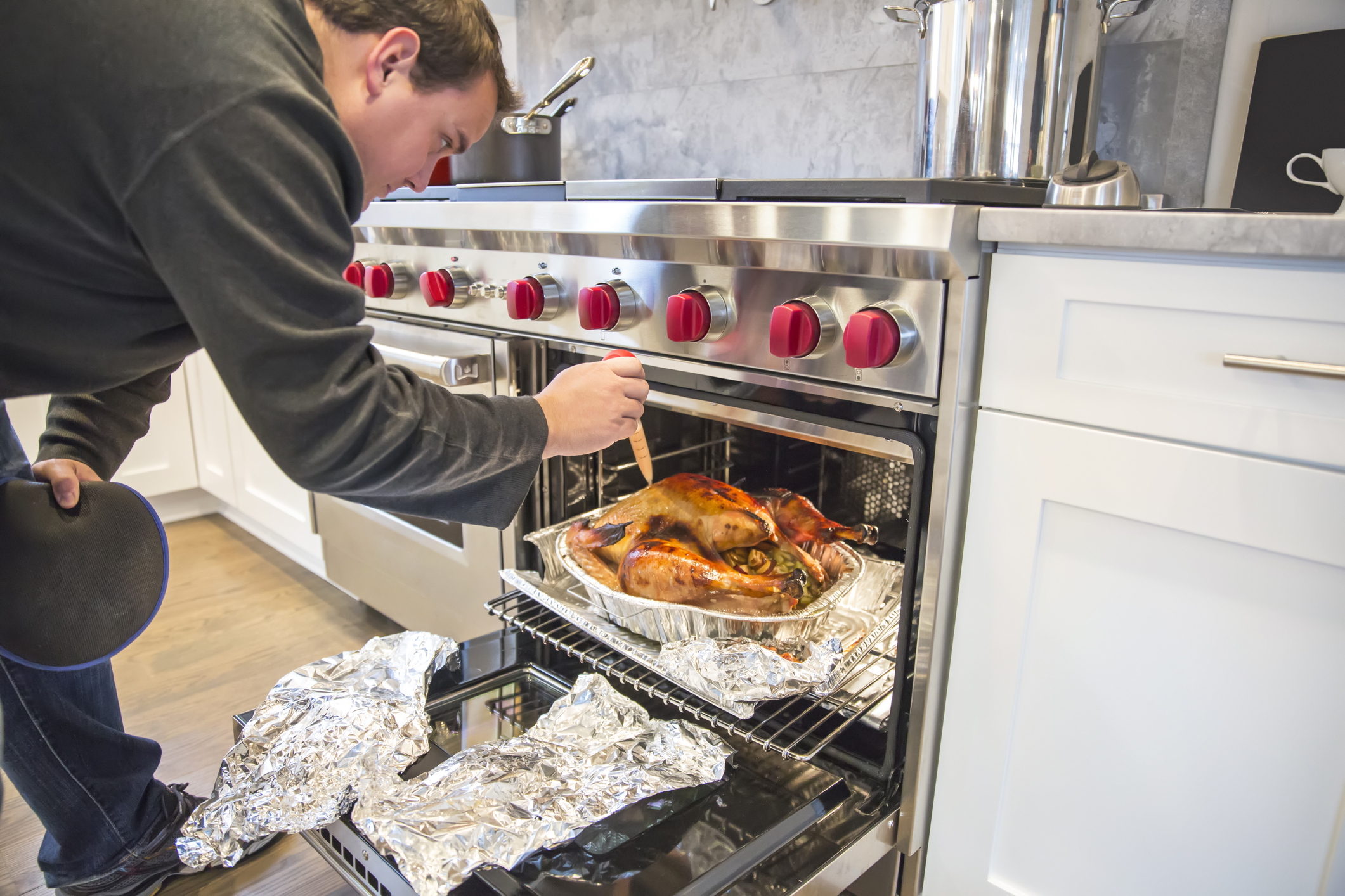 Delicious Thanksgiving turkey is being basted using a plastic baster by man. It is in a tin foil roasting pan. There is stuffing in the turkey and the pan and the giblets are in tin foil next to the pan. Close up shot taken with Canon 5D Mark 3. rm